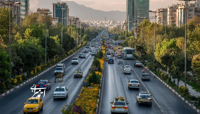 نمایی از بزرگراه شلوغ در تهران با درختان سبز و کوه‌های البرز در پس‌زمینه.
