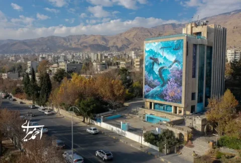 نمایی از خیابانی در شهر با ساختمانی بزرگ که روی دیوارش نقاشی هنری رنگارنگی از پرندگان و طبیعت دیده می‌شود.