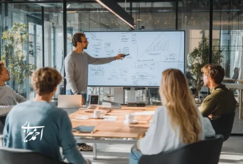 جلسه منتورینگ استارتاپ در یک فضای کاری مدرن، منتور در حال توضیح استراتژی رشد روی وایت‌برد دیجیتال برای تیم بنیان‌گذاران جوان