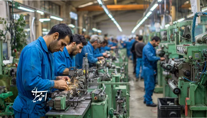 کارگران با لباس آبی در خط تولید کارخانه‌ای صنعتی مشغول کار با دستگاه‌های تراش و ابزارهای فلزی هستند.